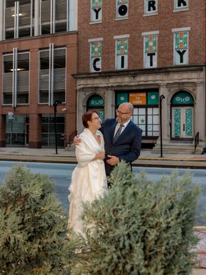 Couple in formal wear embrace outside a brick building with 'York City' signage.