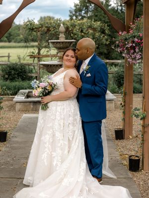 Couple in wedding attire shares romantic moments in outdoor garden setting with wooden pergola structure.