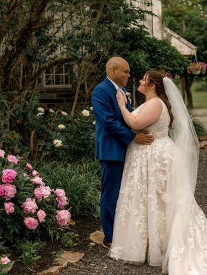 A couple in wedding attire share romantic moments in a garden setting with blooming pink peonies.
