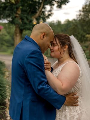 A couple in formalwear shares an intimate kiss outdoors during their wedding photoshoot by a pond with trees in background.