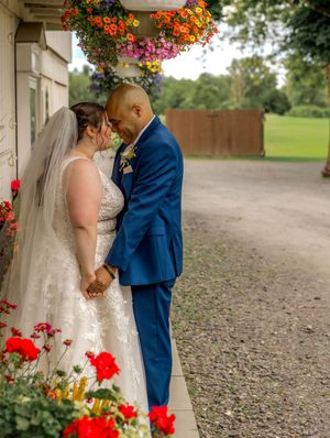 A couple shares an intimate wedding moment surrounded by vibrant red flowers and colorful hanging baskets.