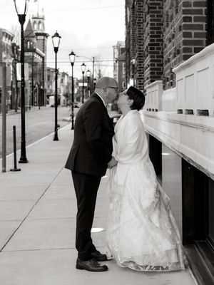 Black and white street scene of a couple in wedding attire near vintage lampposts.