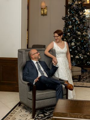 Holiday portrait by a Christmas tree with a person seated in a grey armchair.