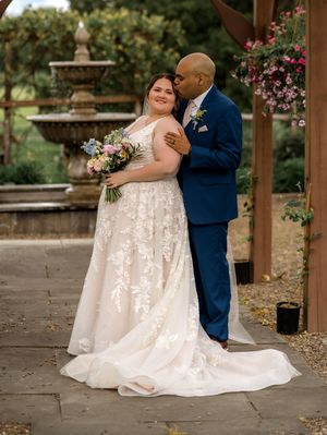 Newlyweds share intimate moments while posing together under a wooden pergola decorated with floral arrangements.