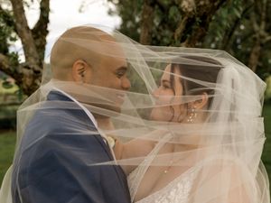 A romantic wedding couple shares a kiss under a flowing veil in an outdoor garden setting.