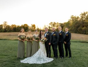 Wedding party members pose together in an outdoor field at golden hour during sunset.