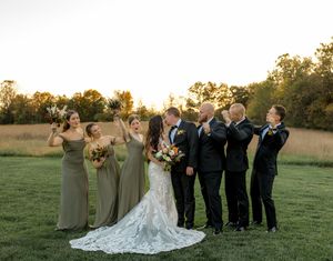 Wedding party stands in formation on a grassy field at sunset while taking professional photos in coordinated attire.
