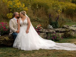 Romantic wedding couple embraces in a scenic autumn garden with golden foliage and blooming flowers in the background.