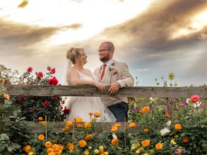 Newlywed couple shares romantic moments in a garden filled with vibrant orange and red flowers at sunset.