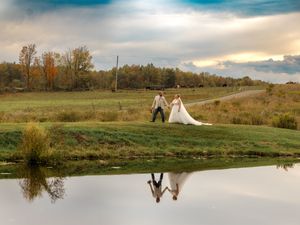 Scenic sunset wedding photos reflected in a tranquil pond with trees and rolling hills in the background.