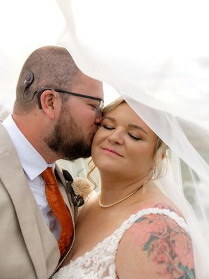 A tender wedding moment under flowing white veil with the couple sharing a gentle kiss.