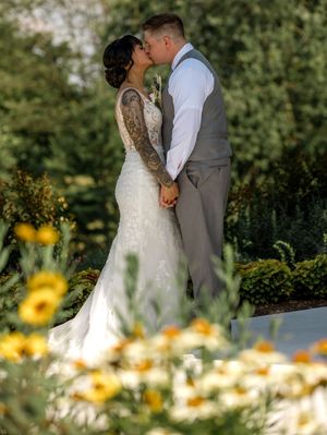 Newlyweds share a romantic kiss in a garden setting with yellow wildflowers blooming in the foreground.