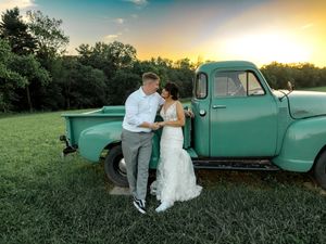Romantic couple poses outdoors during sunset with a vintage mint green pickup truck in a rustic countryside setting.