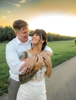 A couple embraces in a romantic sunset moment on their wedding day in a lush green field.