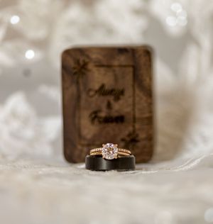 Wedding rings and wooden ring box with a romantic blurred bokeh background and delicate fabric texture.