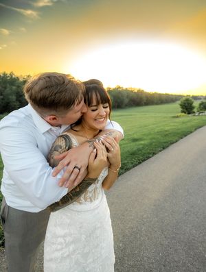 A romantic couple shares tender moments on a dirt path at sunset in a grassy field with soft golden lighting.
