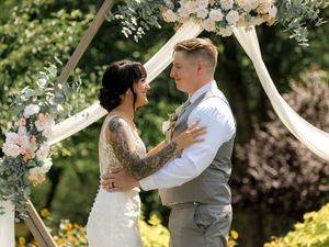 A romantic wedding ceremony outdoors with floral arch decorations, white fabric draping, and natural garden scenery.