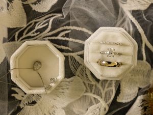 Two octagonal ring boxes displaying engagement and wedding rings on a floral fabric background.