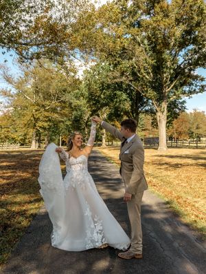 A couple shares a joyful moment dancing together on a tree-lined path covered in autumn leaves.