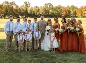 Wedding party poses outdoors in rustic autumn setting with bridesmaids in brown dresses and groomsmen in suspenders.
