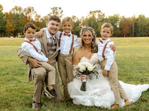 Wedding party poses together on grassy field during golden hour autumn celebration.