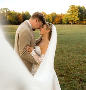 Newlywed couple shares an intimate moment in a field with autumn foliage in the background during golden hour.