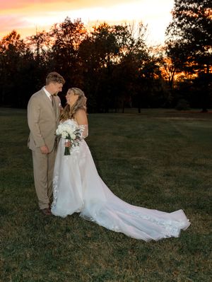 Sunset wedding portraits in a golden field with long flowing white dress and autumn colors in background.