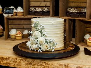 Elegant white wedding cake decorated with fresh flowers and greenery on wooden rustic display.