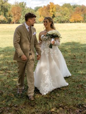 A newlywed couple shares a joyful moment together in an autumn field with fall foliage in the background.