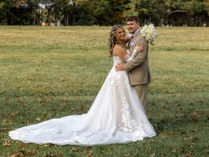 A romantic wedding couple embraces in a sunlit meadow with autumn leaves scattered on the grass.