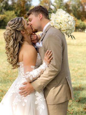A romantic wedding couple embraces in a sun-drenched autumn field with golden foliage in the background.