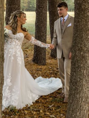 A wedding couple shares a romantic moment among tall trees with fallen autumn leaves in a forest setting.