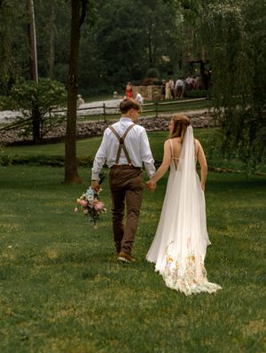 Couple in wedding attire walking through a lush green park on their special day.