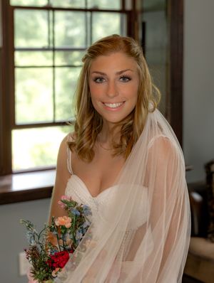 Bride wearing a sweetheart neckline wedding dress with sheer veil holds delicate bouquet featuring peach and red blooms.