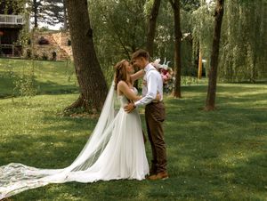 A romantic wedding moment captured outdoors as couple in bridal attire shares a tender moment beneath willow trees.
