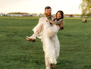 A couple in formal attire joyfully spins and dances together on a sunlit grassy field during golden hour.