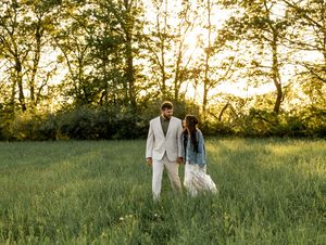 A couple shares a romantic moment in a sunlit meadow during golden hour while dressed in elegant attire.