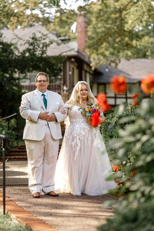 A wedding couple sits together on brick steps in their formal attire amid autumn outdoor garden scenery.