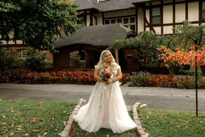 A bride in a flowing white wedding dress twirls joyfully on a lawn with elegant Tudor-style buildings in the background.