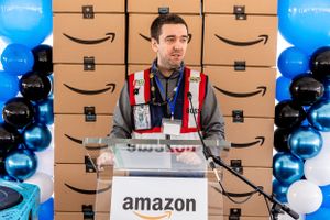 Amazon employee at podium with branded backdrop and balloon decorations.