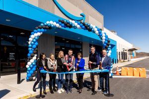 Group gathering under blue and white balloon arch at Amazon facility opening.