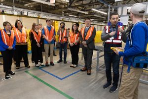 Warehouse employees in safety vests gathered for a training session on factory floor.