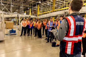 Industrial facility tour group listening to safety briefing in manufacturing area.