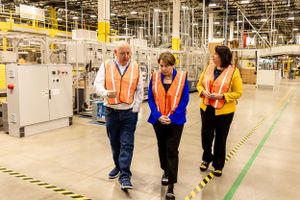 Three workers in safety vests walking along marked lines in manufacturing facility.