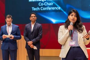 Business professionals speaking at tech conference with blue digital backdrop.