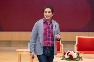 Speaker in casual attire presenting on stage at business conference.
