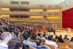 Large auditorium filled with audience members during tech conference presentation.