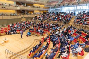 Large concert hall filled with audience members seated in curved rows of red chairs during an event.