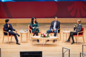 Professional panel discussion with four speakers seated on stage with red backdrop.