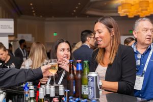 Conference attendees sampling beverages at networking event bar.
